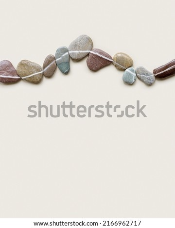 Aesthetic minimal flat lay sea pebble stones with white line, beige background. Composition from natural colored stone on the same level. Balance or harmony concept, top view, horizontal row rocks.