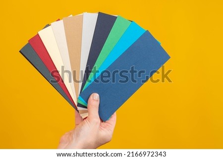 Color palette. Shade swatch cards. Several pastel colors in hand. Designer palette. Concept of design services. Color scheme in female hand. Fan of colored palettes on yellow background