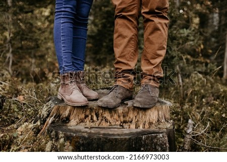 A couple is standing on a wooden trunk and their boots and jeans are on the photo. Close up shot of their trousers and brown footwear. Outdoor lifestyle in the forest.	 Royalty-Free Stock Photo #2166973003