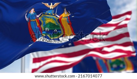The New York state flag waving along with the national flag of the United States of America. In the background there is a clear sky. New York is a state in the Northeastern United States Royalty-Free Stock Photo #2167014077