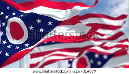 The Ohio state flag waving along with the national flag of the United States of America. In the background there is a clear sky. Ohio is a state in the Midwestern region of the United States