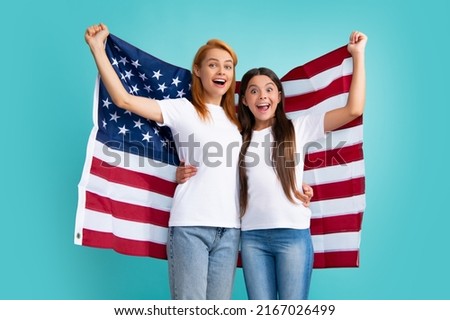 Excited mom and child hold American flag. Patriotic holiday. Happy family, mother and daughter with American flag on blue isolated studio background. USA celebrate independence day 4th of July.