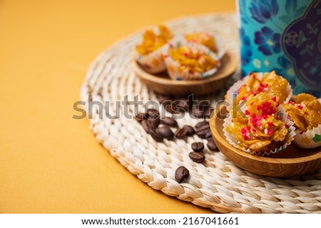 Homemade cornflake cookies with wooden bowls, coffee beans, a coffee cup and a coaster; on orange background. A close-up and selective focus photo of the cookie. A copy space for text or words.