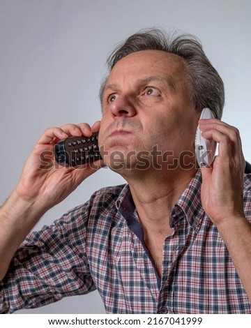 A man with two phones is fed up with being harassed over the phone with unwanted business proposals Royalty-Free Stock Photo #2167041999