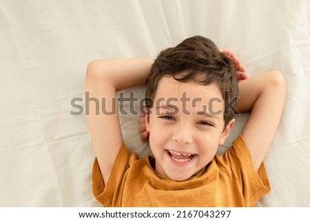 Portrait of a happy smiling child with thick hair. Caucasian brunette boy, toothy smile. Cute kid with milk teeth. Concept of vacation, lice, childhood, dentistry, cotton bed linen. Lifestyle.