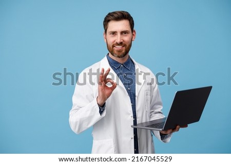 Smiling medical specialist in a white coat holding laptop and showing okey sign