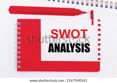 On a white notepad, a red pen, a red notepad and a white sheet of paper with the text SWOT ANALYSIS
