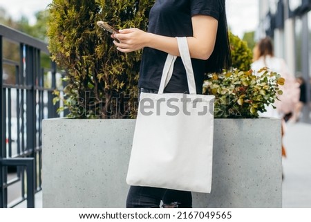 Young model girl on the street holding white eco bag and mobile phone , mock up