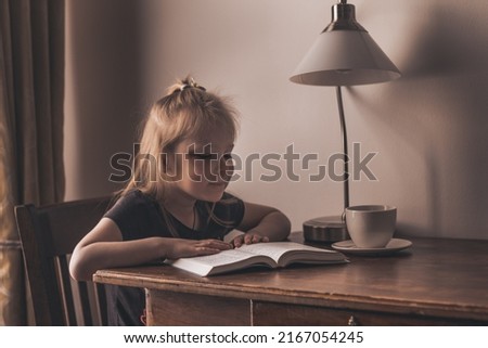 a girl sits at a table reading a book