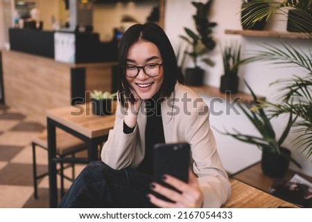 Beautiful millennial asian girl having call on smartphone in cafe. Young smiling brunette woman wearing glasses sitting at table. Concept of rest, leisure and free time. Modern female lifestyle