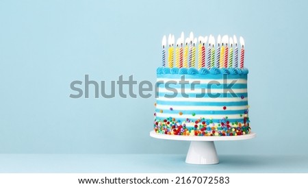 Striped buttercream birthday cake with colorful birthday candles and sprinkles on a blue background Royalty-Free Stock Photo #2167072583