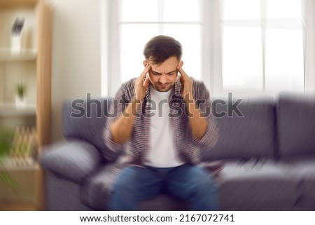 Man suddenly feels dizzy and takes a seat on the sofa. Young guy feeling pain and spinning sensation in his head. Headache, vertigo, health problem, brain tumor concept Royalty-Free Stock Photo #2167072741