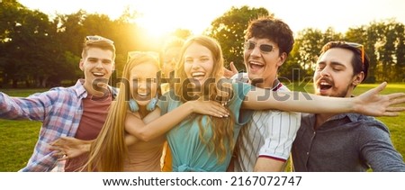 Group of six best friends have fun and laugh out loud while walking in park on summer sunny day. Cheerful multiracial young men and women have fun together outdoors. Youth culture concept. Web banner.