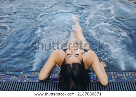 A beautiful fashionable woman in bikini posing on the blue hot tube background