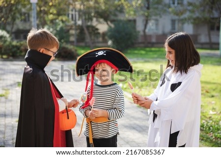 Treat or trick! Outdoor shot of three kids wearing carnival costumes for Halloween sharing candies with each other. Holiday celebration and Halloween traditions concept.