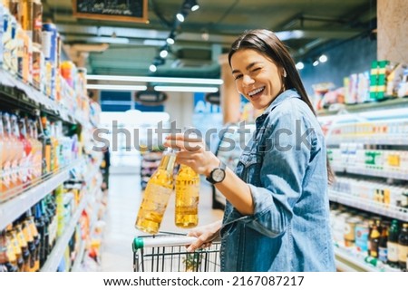 Portrait joyful young woman buying beer in liquor store holding two bottles in her hand winking cheerfully smiling looking at camera Royalty-Free Stock Photo #2167087217