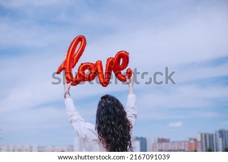 A woman with black curly hair holds in her hands a balloon in the shape of the word love. Congratulations on the holiday of loved ones. A romantic declaration of love. Valentine's Day Celebrations