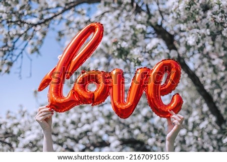 Festive balloon of red color. Hands hold the inscription love against the sky and trees. Happy birthday. Celebrating Valentine's Day