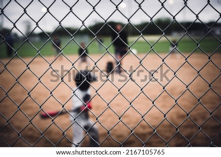 Selective focus on chain link fence with a youth baseball game defocused and blurred in the background