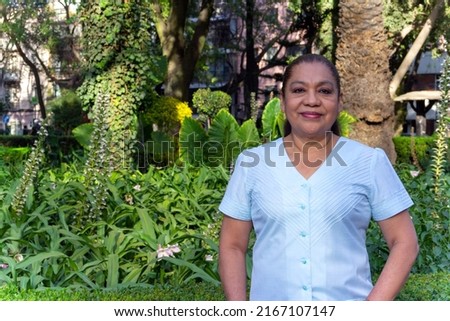 Mature Mexican woman looking at camera, smiling, standing in front of a garden. Latin woman looking at camera smiling. cheerful attitude. Royalty-Free Stock Photo #2167107147