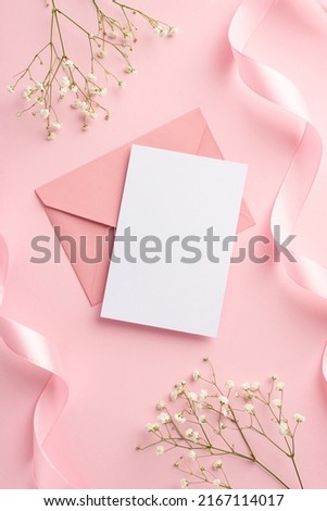 Wedding invitation concept. Top view vertical photo of pink envelope paper sheet silk curly ribbons and white gypsophila flowers on isolated pastel pink background with blank space