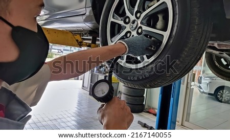 An Indonesian car mechanic is checking tire pressure of a wheel during car is on a lift in an authorized workshop dealership