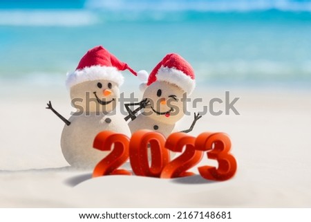Two Sandy Christmas Snowmen are celebrating a Happy New Year on a beautiful beach with 2023 3d text, concept for new year 2023 Royalty-Free Stock Photo #2167148681