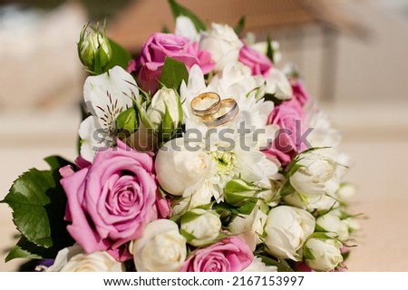 Composition with the bride's bouquet of pink roses and wedding rings visible from a high angle