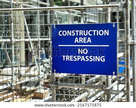 Blue construction area no trespassing sign hang on metal fence of construction site.