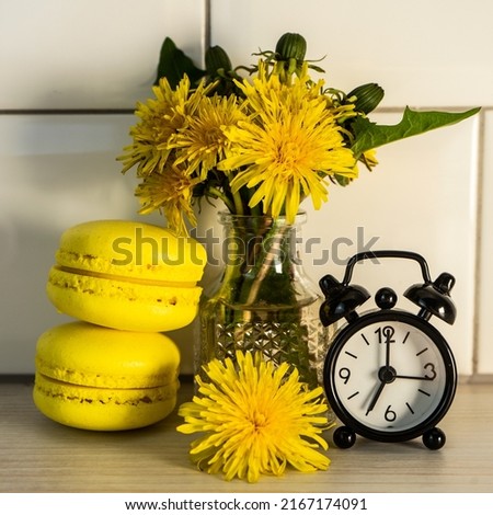 Macaroons, yellow dandelions and an alarm clock. Good morning. French cookies on the table and yellow dandelions. Selective focus.