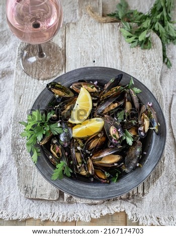 Mussels prepared with white wine, butter, garlic, lemon and herbs; served on a rustic black ceramic plate with rosé wine
Top view Royalty-Free Stock Photo #2167174703