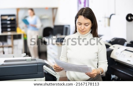 Portrait of an attentive woman checking the quality of printing in a printing house