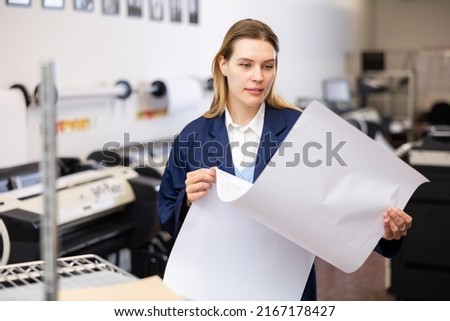 Woman checking large format paper after printing. Press worker looking at paper. Royalty-Free Stock Photo #2167178427