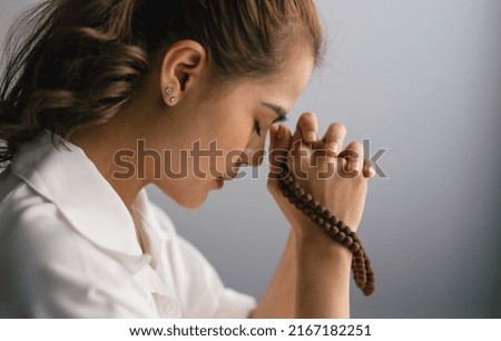 Beautiful young woman praying with hands together on gray background at home. Asian woman pray for god blessing wishing better life.