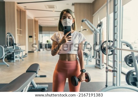 concept of sport, fitness, lifestyle, technology, and people - young woman taking a picture in the gym mirror with her smartphone