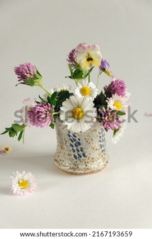 Small bouquet of wild flowers in a vase on a gray background. Daisies, clover, pansies. Selective focus on a daisy, natural light. vertical image