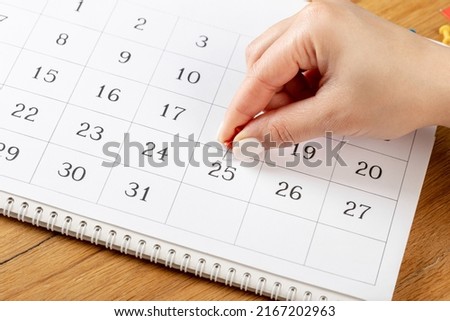 red Hand pin stuck on the day of the month in the calendar, business concept. beautiful female hand fingers Royalty-Free Stock Photo #2167202963