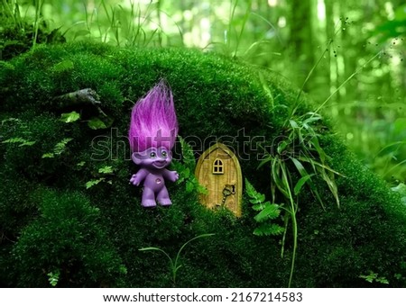 cute tale troll and little wooden door in mystery forest, natural green background. funny troll toy with ruffled violet hair. fairytale beautiful magic atmosphere. template for design