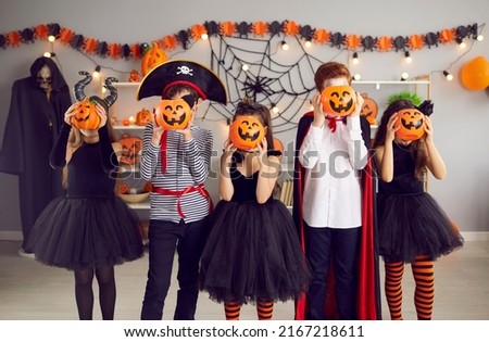 Group of small teenage children dressed in costumes for Halloween party in school. Happy kids pose with jack-o pumpkins have fun celebrate spooky all saints eve holiday in decorated kindergarten.