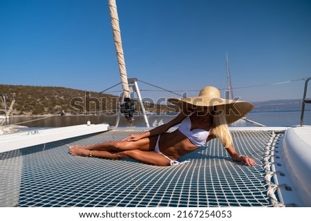 Beautiful young blond woman in bikini laying on catamaran bow at sunny summer day