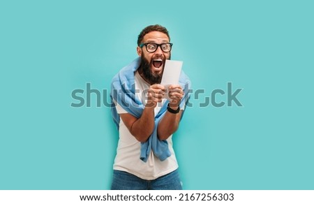 Excited happy young male winner feeling joy winning lottery, placing bets, getting cashback online gift isolated on blue background. Human face emotions and betting concept. Trendy colors Royalty-Free Stock Photo #2167256303