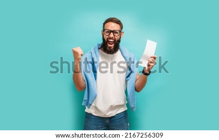 Excited happy young male winner feeling joy winning lottery, placing bets, getting cashback online gift isolated on blue background. Human face emotions and betting concept. Trendy colors Royalty-Free Stock Photo #2167256309