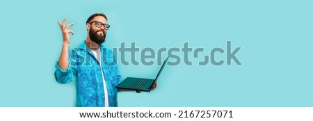 Young crazy bearded charismatic man. Shocked or surprised expression. Laptop concept. Funny promotion poster. Programmer, web developer holding a laptop in his hands and looking at the camera Royalty-Free Stock Photo #2167257071