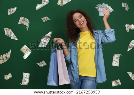 Happy young African American woman with shopping bags and money and falling American dollars on green background