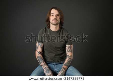 Young man with tattoos on arms against black background