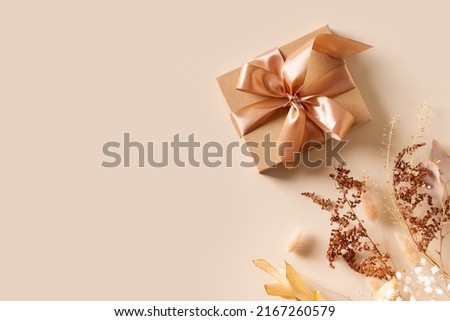 Gift box with golden ribbon and dry grass and flowers on beige background flat lay, top view, copy space Royalty-Free Stock Photo #2167260579