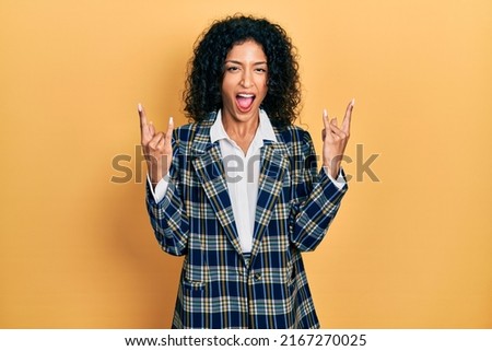 Young latin girl wearing business clothes shouting with crazy expression doing rock symbol with hands up. music star. heavy concept. 