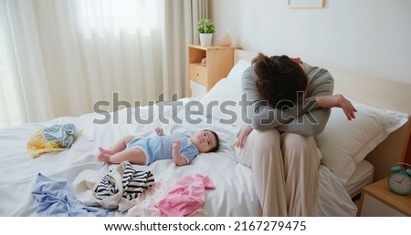 authentic shot of asian mother has postpartum depression with her baby who is lying on bed 
