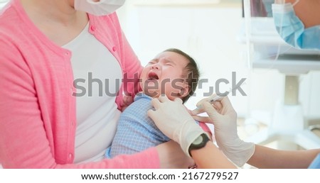 authentic shot of asian mother and infant in pediatrics clinic - doctor wearing face mask inject vaccine to a baby who is hold by mom Royalty-Free Stock Photo #2167279527
