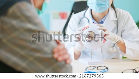 close up of asian female doctor wearing face mask is showing eyeball model and explaining about eyes disease to elder senior man patient in hospital Royalty-Free Stock Photo #2167279565